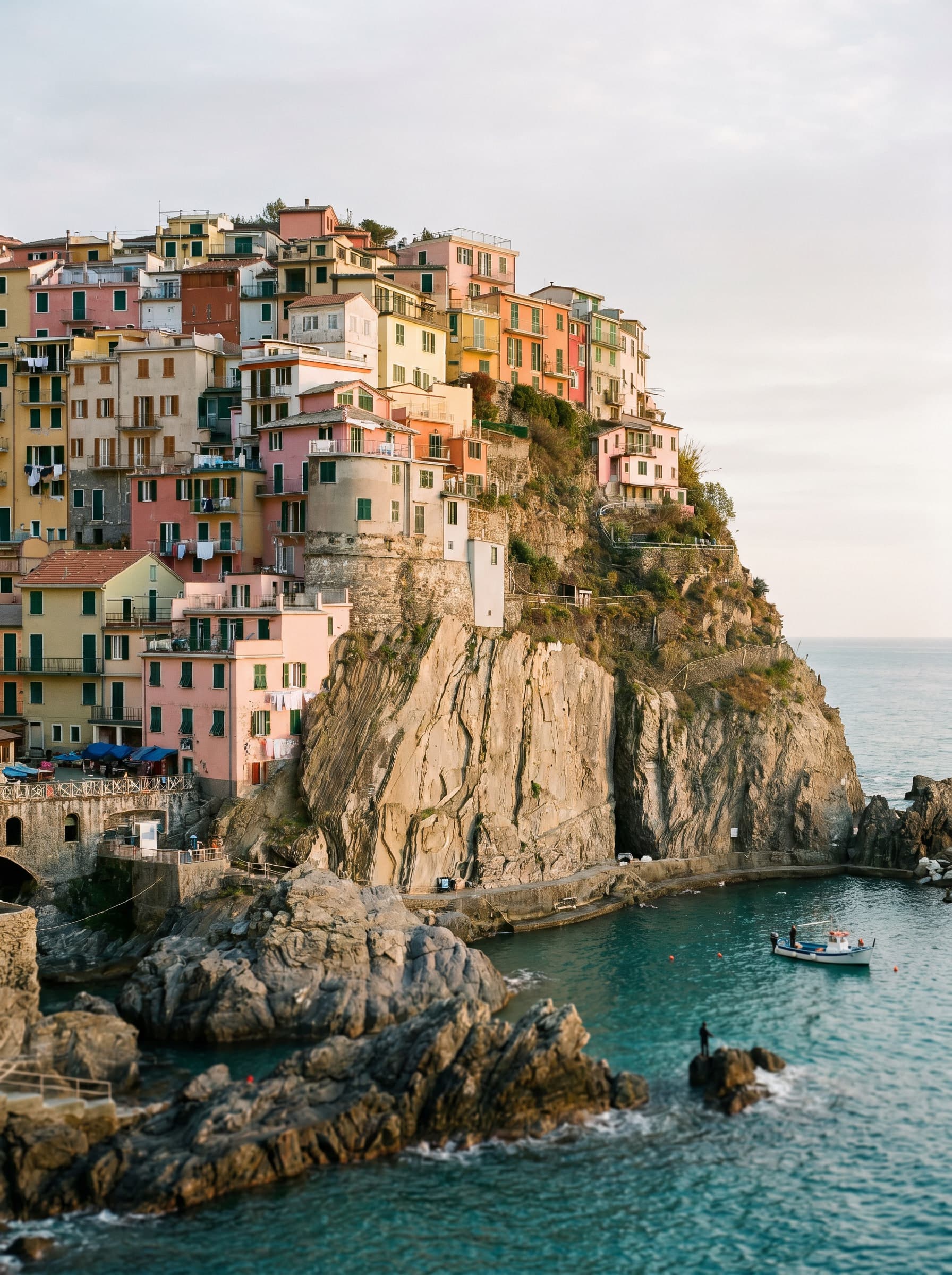 A pastel Ligurian fishing village clinging to a cliff above the turquoise Mediterranean, a distant fishing boat in the harbour